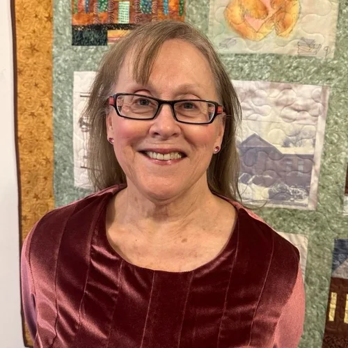 Linda Georgeson standing in front of a quilt smiling