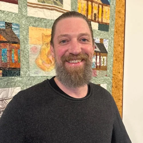 Ryan Hogan standing in front of a quilt smiling