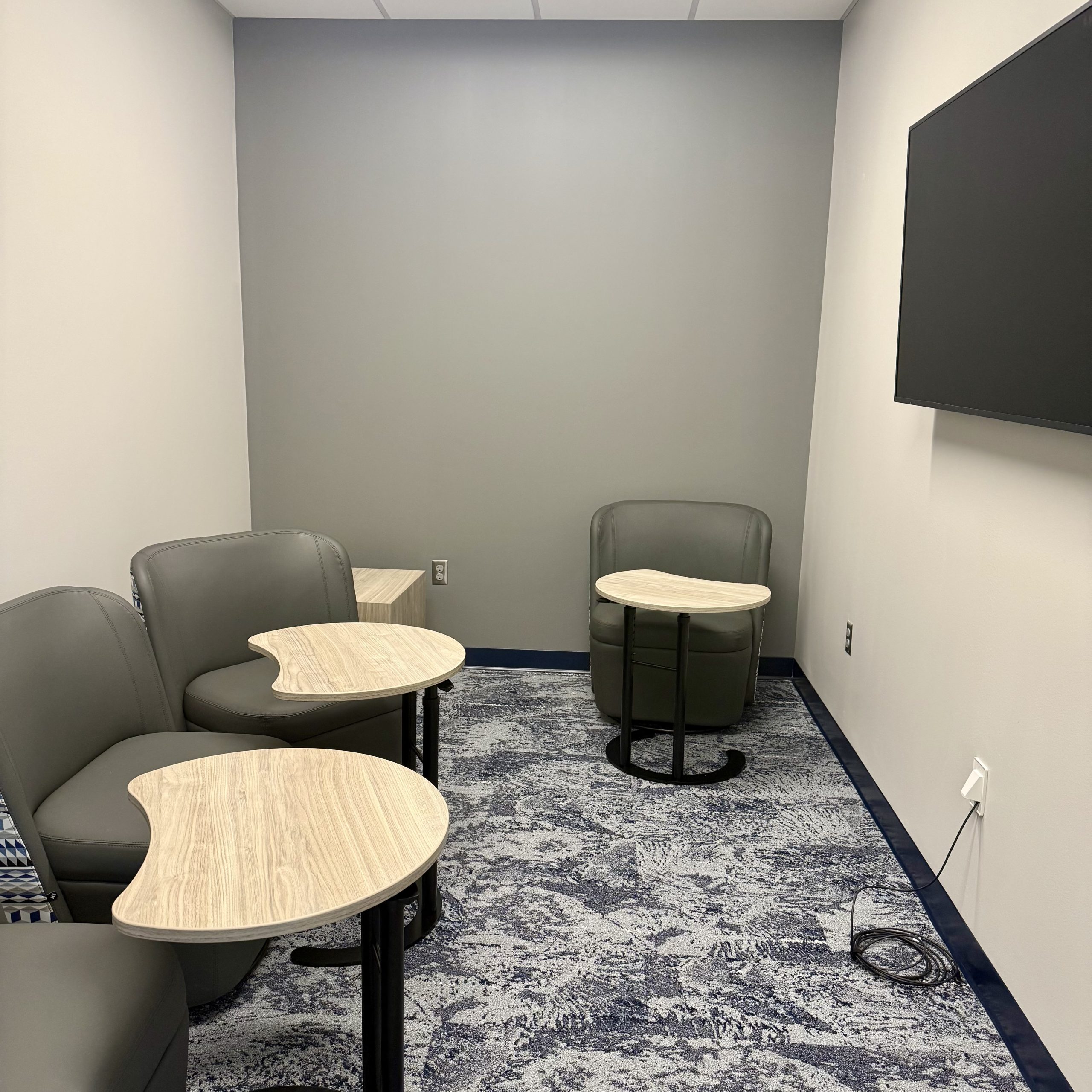 meeting room with lounge chairs, small tables and tv screen