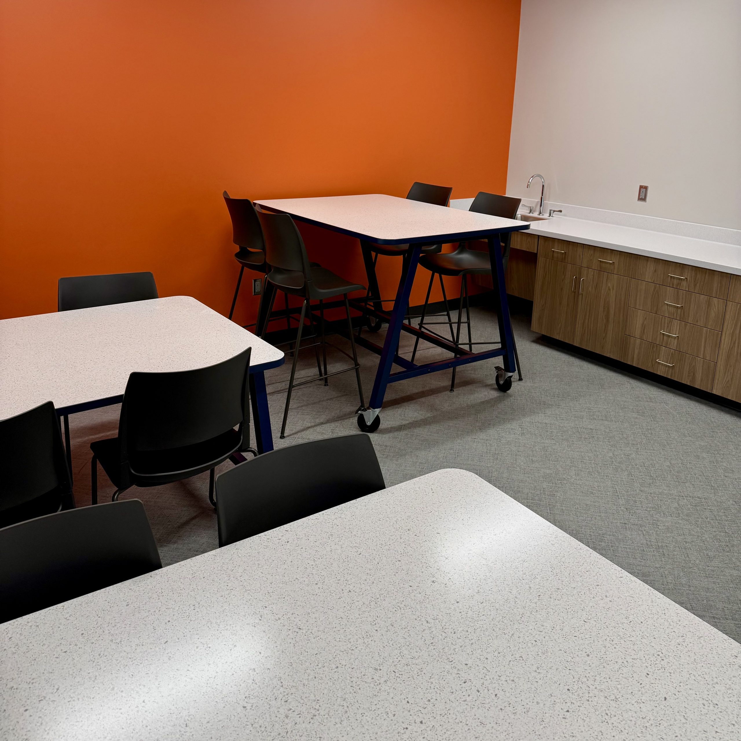 work room with tables, chairs, orange wall, counter and sink