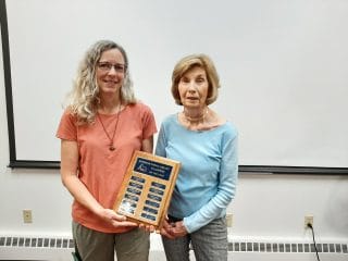 Two women holding a plaque in front of a whiteboard