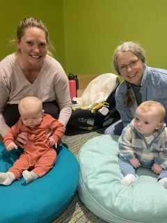 Two mothers posing with their two babies who or sitting on beanbag chairs