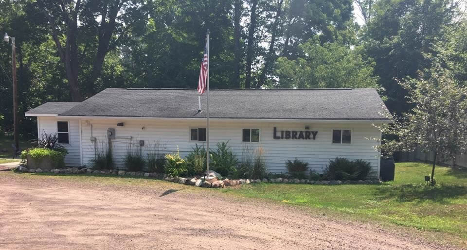 Small white library building with a flagpole and surrounding greenery.