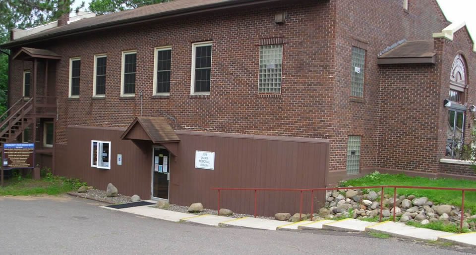 A two-story brick building with a brown wooden annex, featuring several windows and an external staircase.